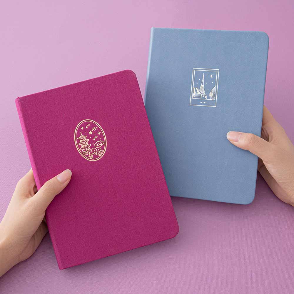 A pair of hands holding a Tsuki Kyoto bullet journal and Tokyo bullet journal