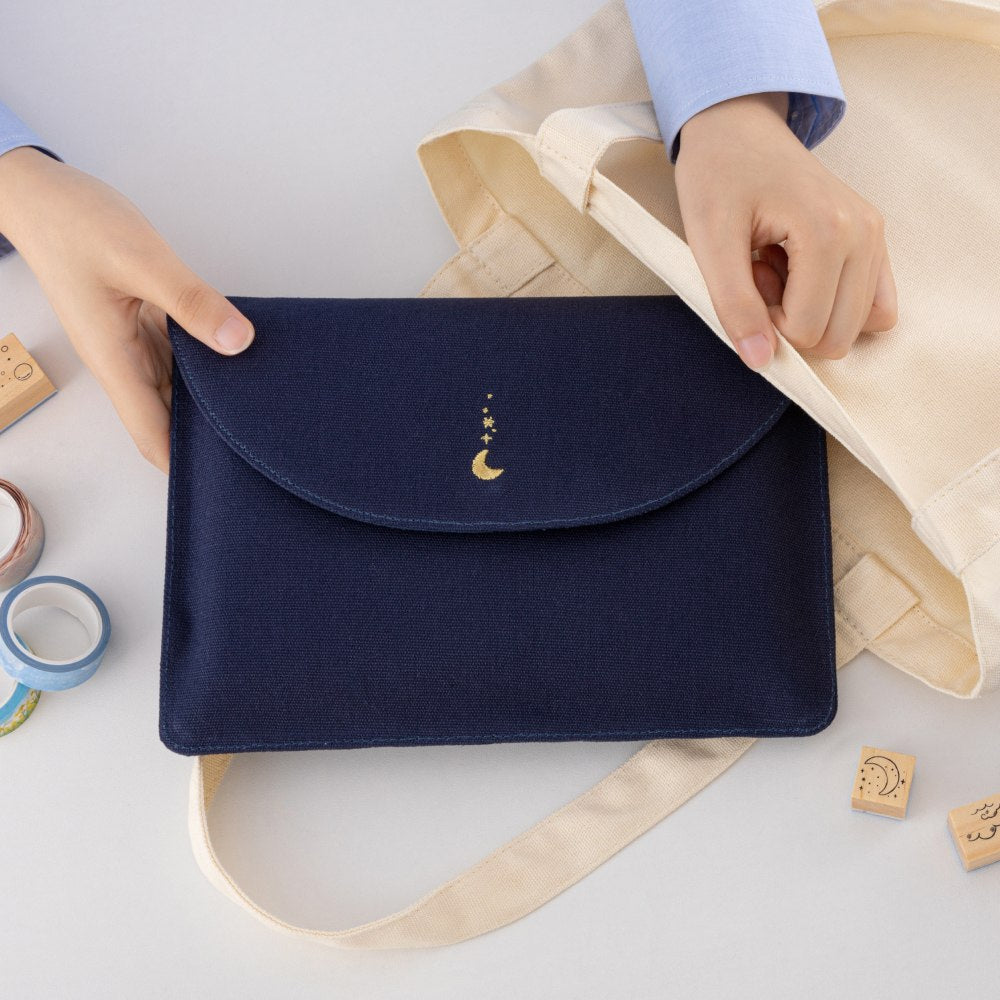 Hands putting Cloud Dreamland notebook pouch in a tote bag