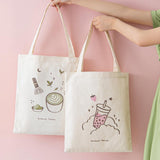 Tsuki ‘Ichigo’ Boba Tote Bag held in hands with Tsuki ‘Matcha Matcha’ Tote Bag in light pink background