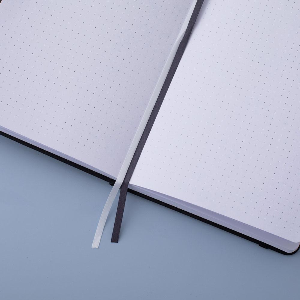 Deep black Tsuki Playful Orca limited edition bullet journal on open page with two bookmark ribbons on blue background