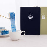 Tsuki ‘Cup of Galaxy’ Washi Tapes in teacup and on saucer with Tsuki ‘Cup of Galaxy’ Limited Edition Holographic Bullet Journal and Tsuki ‘Matcha Matcha’ Limited Edition notebook on linen covered table