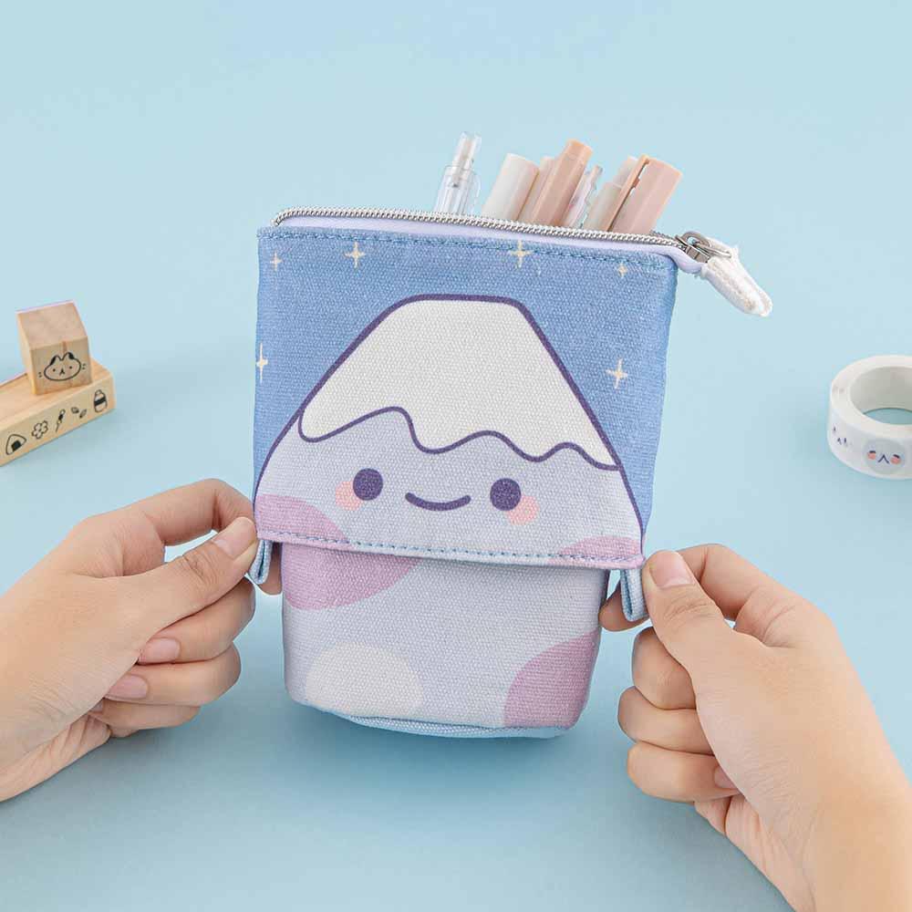 Tsuki ‘Four Seasons’ Fuji Pop-Up Pencil Case by Notebook Therapy x Milkkoyo held in hands with Tsuki ‘Four Seasons’ Washi Tapes and Tsuki ‘Four Seasons’ Bullet Journal Stamps on light blue background