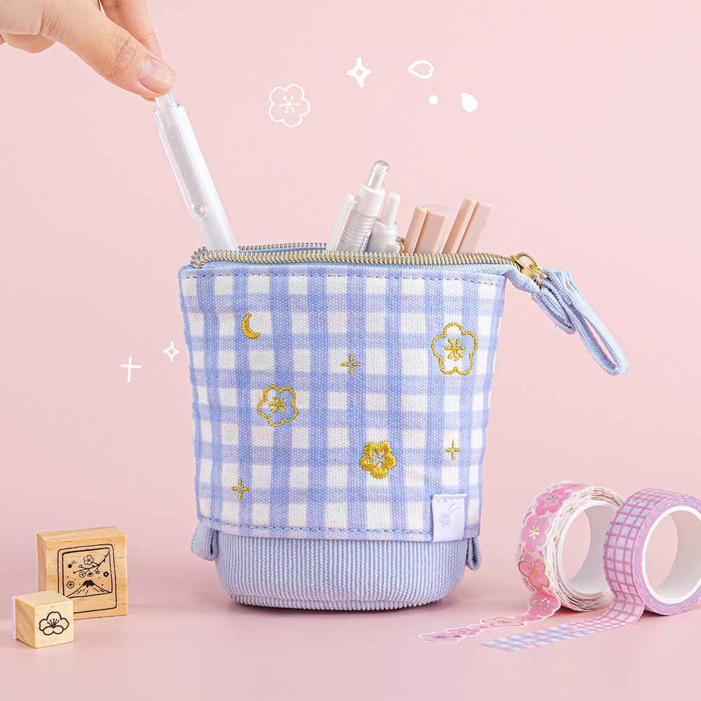Tsuki ‘Sakura Journey’ Pop-Up Pencil Case with pens inside held in hands with Tsuki ‘Sakura Journey’ Washi Tape Set and Tsuki ‘Sakura Journey’ Bullet Journal Stamps in light pink background