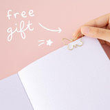 Close up of open page of Tsuki Cloud White ‘Flutter + Dream’ Limited Edition Bullet Journal by Notebook Therapy x Pelinkan with free butterfly bookmark gift held in hand in pastel pink background