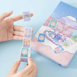 Tsuki ‘Four Seasons’ Stamp Washi Tape by Notebook Therapy x Milkkoyo held in hands with Tsuki ‘Four Seasons: Winter Edition’ Bullet Journal on light blue background