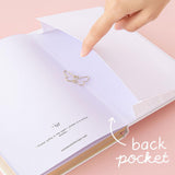 Close up of open back page pocket of Tsuki Cloud White ‘Flutter + Dream’ Limited Edition Bullet Journal by Notebook Therapy x Pelinkan with free butterfly bookmark gift held in hand on pastel pink background
